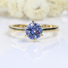 a yellow gold ring with a tan sapphire in the center and white flowers in the background