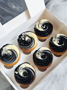 six cupcakes with white and black frosting in a box on a table