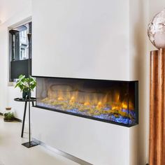 an electric fireplace in the middle of a living room with white walls and floor to ceiling windows