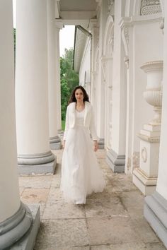 a woman in a white dress is walking down the sidewalk with columns on either side