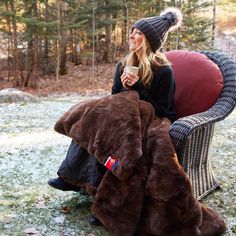 a woman sitting in a chair with a blanket on it and holding a coffee cup