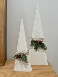 two white wooden christmas trees with evergreen and red berries tied to them on a table