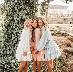 three girls are posing for the camera in front of a tree with their arms around each other