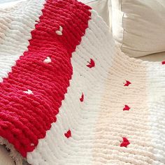 a red and white crocheted blanket sitting on top of a bed next to pillows