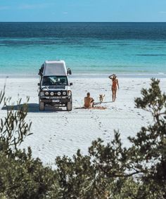 two people and a dog are on the beach with a truck parked in front of them