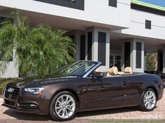 a brown convertible car parked in front of a building with palm trees and cars behind it