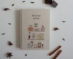 a recipe book surrounded by spices and cinnamons on a white surface with star anise scattered around it