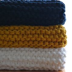 three crocheted towels are stacked on top of each other, one is blue and the other is yellow