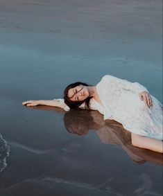 a woman is laying on the beach with her legs spread out in the water and she is wearing a white dress