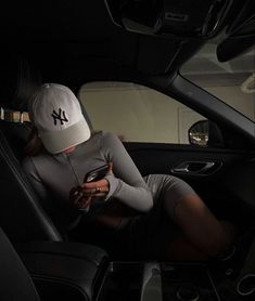 a woman sitting in the back seat of a car looking at her cell phone while wearing a new york yankees hat