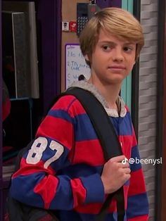 the young boy is wearing a red and blue striped sweater while standing in front of a door