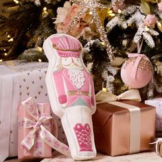 a pink and white vase sitting next to presents under a christmas tree with lights on it