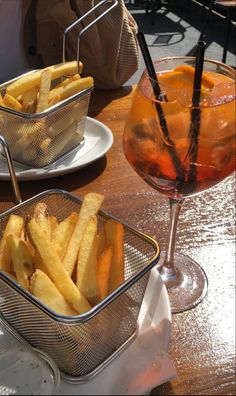 french fries are in baskets next to a glass of wine on a table with other plates and glasses