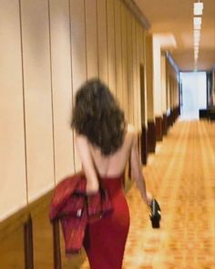 a woman in a red dress is walking down the hall with her hand on her hip