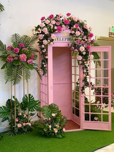 a pink phone booth decorated with flowers and greenery