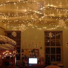 a bedroom with lights strung from the ceiling and a laptop computer sitting on top of it