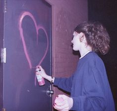 a woman writing on a wall with spray paint and a pink heart drawn on it