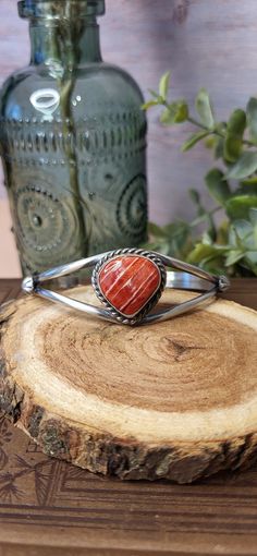 This gorgeous Split Shank Cuff Bracelet is made by Navajo Silversmith Artist Augustine Largo with Spiny Oyster.  The vibrant pinkish orange stone is set into a smooth vintage patina sterling silver bezel and surrounded by a beautiful twisted rope design and starburst on each side of the split shank cuff.   Spiny Oyster is often used in Native American Jewelry and is believed to bring good fortune and fertility making this the perfect gift for a friend or spouse for any special occasion! ★Specifics★ Metal: Sterling Stamped Size of Bracelet:  As the piece sets it will fit a 6 1/2" wrist and can be slightly adjusted up or down. Gap: 1 1/4" Width: 7/8" at most widest point, 1/4" at most narrow point Weight of Bracelet: 16g Hallmarked: AL (Augustine Largo) ★  Free shipping on all orders! We shi Southwestern Inlay Cuff Bracelet Gift, Southwestern Style Sterling Silver Bracelet, Handmade Southwestern Sterling Silver Bracelet, Western Style Cuff Bangle Bracelet Gift, Southwestern Adjustable Cuff Bracelet With Natural Stones, Southwestern Cuff Bracelet With Natural Stones As Gift, Southwestern Natural Stones Cuff Bracelet Gift, Southwestern Bangle Cuff Bracelet With Natural Stones, Southwestern Style Natural Stones Cuff Bangle