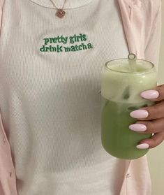 a woman holding a green drink in her right hand and wearing a white shirt with the words pretty girls drink matcha on it