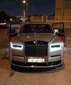 the front end of a silver rolls royce parked in a parking lot at night with its doors open