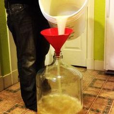 a person is pouring water into a large glass bottle with a red funnell on top