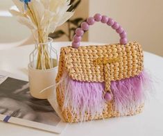 a straw bag with pink and purple feathers on the handle sits next to a vase filled with flowers