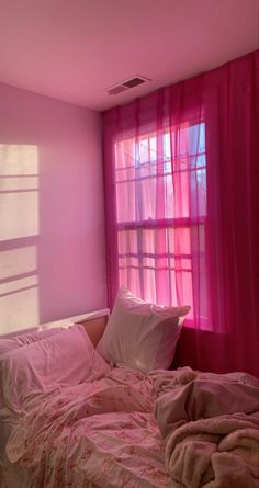 a bed with pink sheets and pillows in front of a window