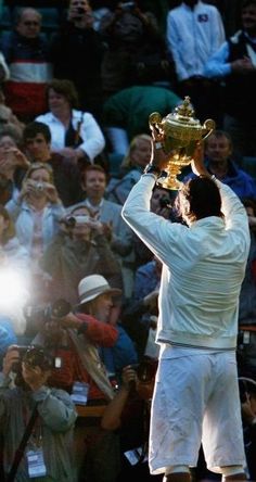 a man holding up a tennis trophy in front of a group of people watching him