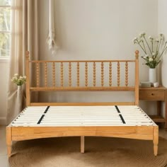 a wooden bed frame sitting on top of a rug next to a table with flowers