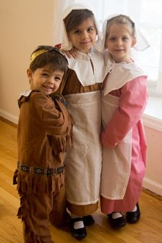 three children dressed in costumes standing next to each other on a wooden floor near a window