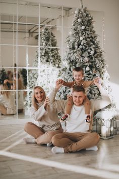 a man, woman and child sitting on the floor in front of a christmas tree