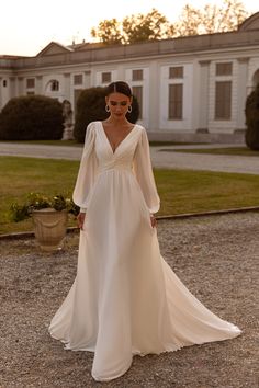 a woman in a white wedding dress standing on top of a gravel road next to a building