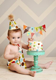 a baby sitting on the floor in front of a cake and wearing a party hat