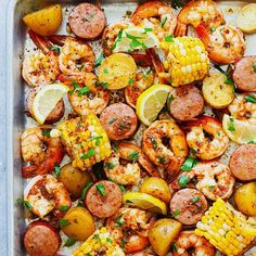 a pan filled with shrimp, potatoes and corn on the cob next to lemon wedges