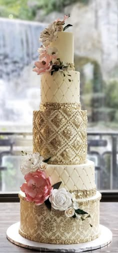 a three tiered wedding cake with flowers on the top and gold trimmings