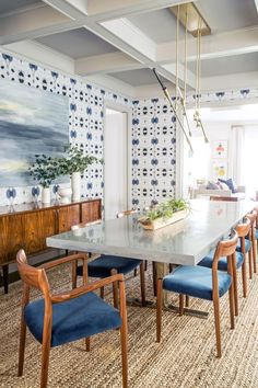 a dining room table with blue chairs and a painting on the wall in the background