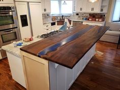 a kitchen with an island made out of wood in the center and stainless steel appliances on the other side