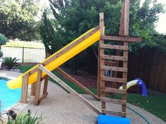 a wooden play set with a slide and pool in the background