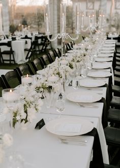 a long table is set with white plates and silverware for an elegant wedding reception