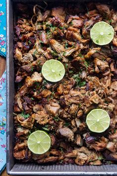 a pan filled with meat and limes on top of a table