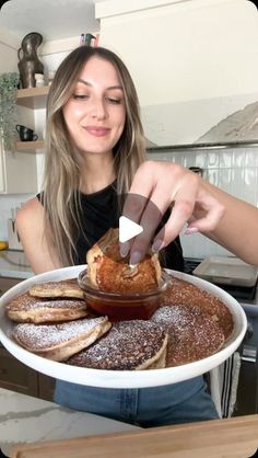 a woman holding a plate with french toast and powdered sugar on it in the kitchen