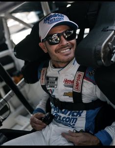 a man sitting in the drivers seat of a race car wearing sunglasses and a hat