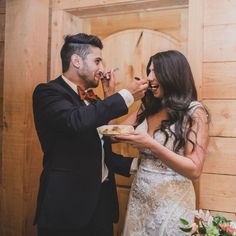 a bride and groom feeding each other cake at their wedding reception in front of a wooden wall