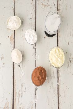 four measuring spoons with different types of food in them on a white wooden surface