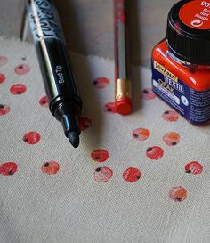 two pens and an ink bottle on a table cloth with red flowers in the background