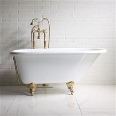 an old fashioned bathtub in front of a white brick wall with gold faucet handles