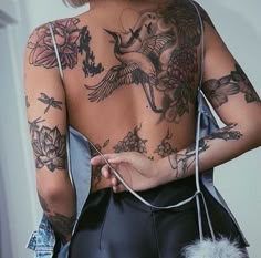 the back of a woman with tattoos on her body, holding a feather in her hand