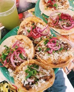 three tacos with meat, onions and cilantro sitting on a green plate