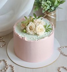 a pink cake with white flowers on top sitting on a plate next to a plant