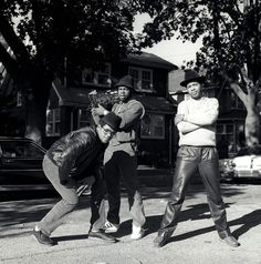 three men are standing on the street and one is holding a baseball bat in his hand